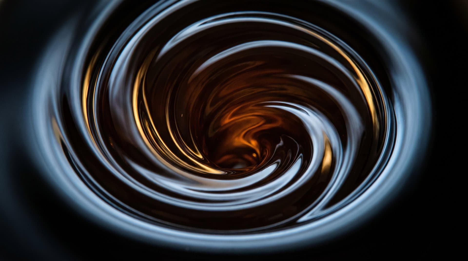 Amber motor oil turning in a slow vortex, lit against carbon black